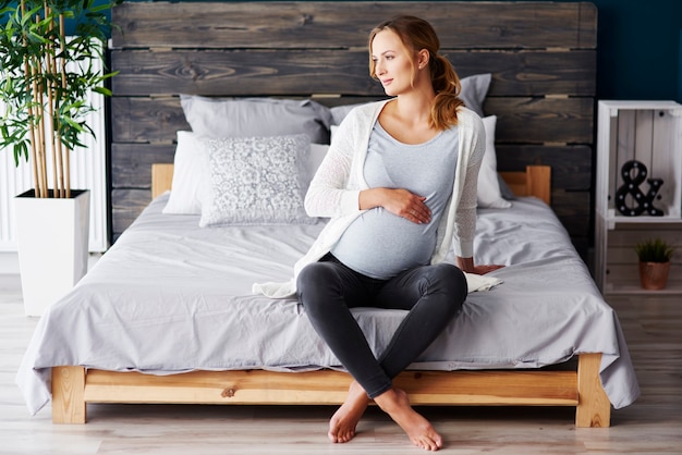 Retrato de mujer embarazada descansando en el dormitorio