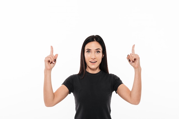 Retrato de una mujer emocionada feliz apuntando dos dedos hacia arriba