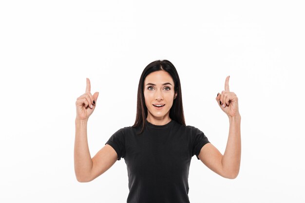 Retrato de una mujer emocionada feliz apuntando dos dedos hacia arriba