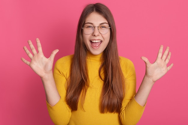 Retrato de mujer emocionada feliz vistiendo atuendo casual amarillo y gafas, levantando las palmas hacia arriba, expresando emociones positivas