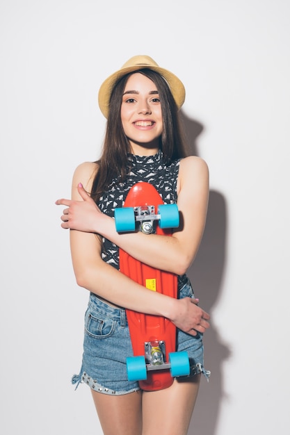 Foto gratuita retrato de una mujer emocionada sonriente agujereando el monopatín aislado en la pared blanca