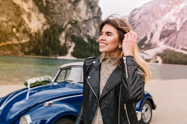 Foto gratuita retrato de mujer emocionada tocando su cabello y mirando a otro lado con una sonrisa caminando cerca del lago