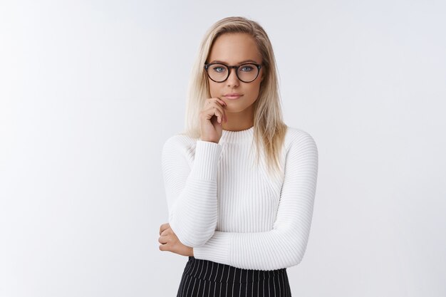 Foto gratuita retrato de mujer emprendedora enfocada y de aspecto serio que trabaja pensando en una oferta interesante y arriesgada tocando el labio y mirando determinada a la cámara, tomando una decisión sobre el fondo blanco.