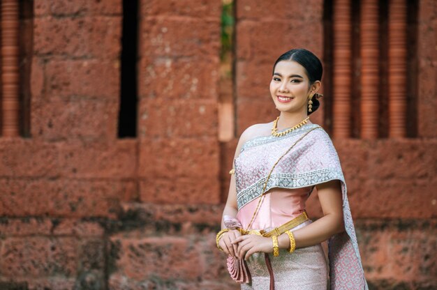 Retrato de mujer encantadora asiática vistiendo un hermoso vestido típico tailandés identidad cultura de Tailandia en el templo antiguo o lugar famoso con pose graciosamente