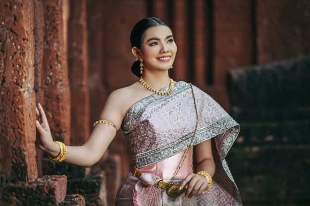 Retrato de mujer encantadora asiática vistiendo un hermoso vestido típico tailandés identidad cultura de Tailandia en el templo antiguo o lugar famoso con pose graciosamente