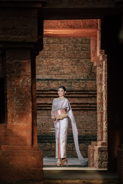 Retrato de mujer encantadora asiática vistiendo un hermoso vestido típico tailandés identidad cultura de Tailandia en el templo antiguo o lugar famoso con pose graciosamente