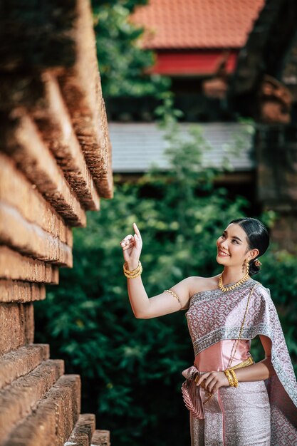 Retrato de mujer encantadora asiática vistiendo un hermoso vestido típico tailandés identidad cultura de Tailandia en el templo antiguo o lugar famoso con pose graciosamente