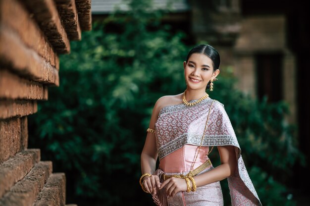 Retrato de mujer encantadora asiática vistiendo un hermoso vestido típico tailandés identidad cultura de Tailandia en el templo antiguo o lugar famoso con pose graciosamente