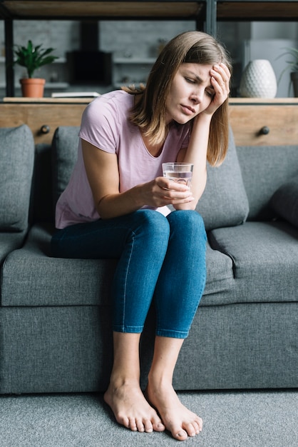 Retrato de una mujer enferma sentada en el sofá con vaso de agua