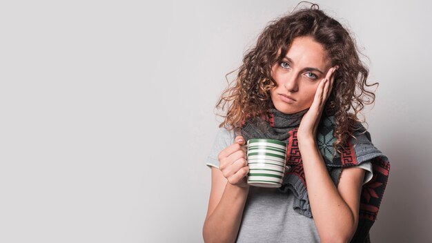 Retrato de mujer enferma con taza de café sobre fondo gris