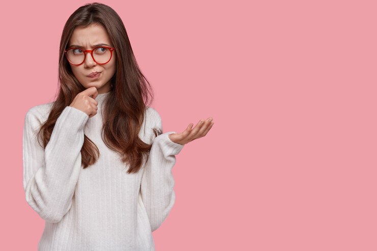Foto gratuito retrato de mujer enojada tiene la mano debajo de la barbilla, frunce los labios y gesticula con enojo, usa suéter blanco, insatisfecho con el precio en la tienda, mira a un lado