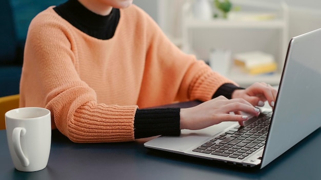 Retrato de una mujer escribiendo en una laptop y sonriendo a la cámara, haciendo trabajo de clase en línea para crear un proyecto de investigación para la tarea escolar. Información de asignación de planificación para adultos jóvenes en la computadora.