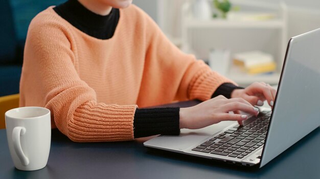 Retrato de una mujer escribiendo en una laptop y sonriendo a la cámara, haciendo trabajo de clase en línea para crear un proyecto de investigación para la tarea escolar. Información de asignación de planificación para adultos jóvenes en la computadora.
