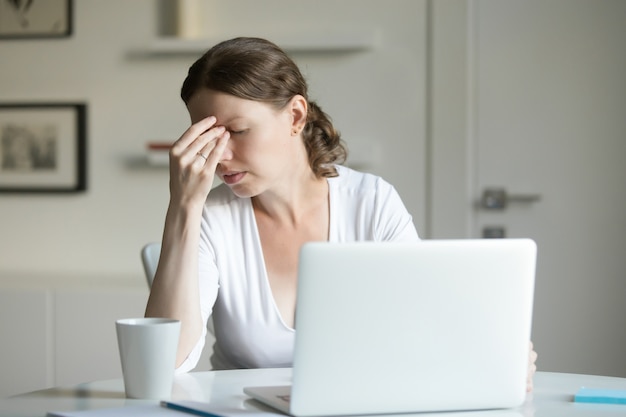 Retrato de una mujer en el escritorio con la computadora portátil, la mano en la frente