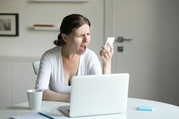 Retrato de una mujer en el escritorio con el portátil, mirando el móvil