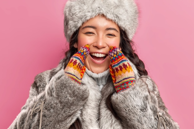 Foto gratuita retrato de mujer esquimal feliz alegre viste abrigo de invierno y guantes de punto exclama alegremente mira positivamente al frente vive en el lejano norte aislado sobre pared rosa