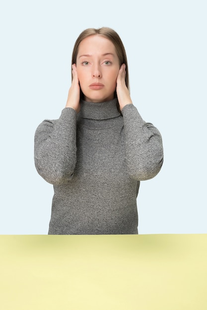 Retrato de mujer estresada sentada con los ojos cerrados y cubriendo con las manos. Aislado en el fondo azul del estudio.