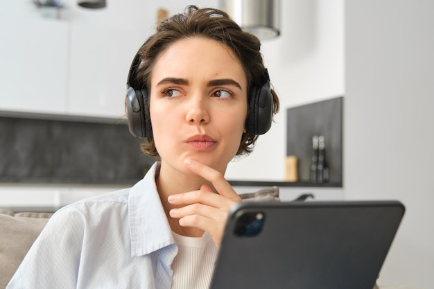 Retrato de mujer estudiando escuchar música en auriculares pensando mientras trabaja en tableta digital wo