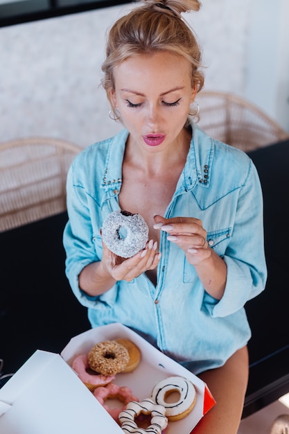 Foto gratuita retrato de mujer europea con cabello rubio disfrutando de donuts en la cocina en casa villa.