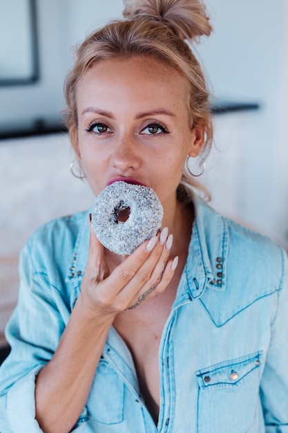 Retrato de mujer europea con cabello rubio disfrutando de donuts en la cocina en casa villa.