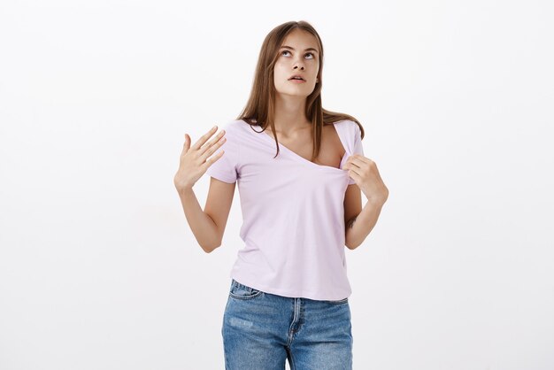 Retrato de mujer europea linda disgustada que sufre de verano tirando de la camiseta y haciendo viento con la palma para refrescarse mientras camina bajo el sol mirando hacia arriba irritado