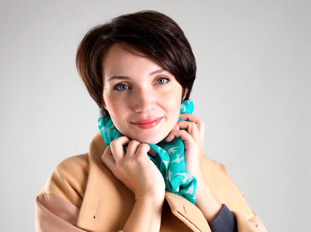 Retrato de mujer feliz en abrigo beige de otoño con pañuelo verde sobre fondo gris