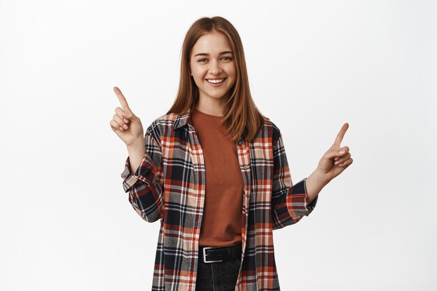 Retrato de mujer feliz apuntando a la venta, mostrando descuentos de lado, dos opciones, variantes de artículos con descuentos, sonriendo a la cámara, fondo blanco