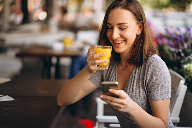 Retrato de una mujer feliz en un café con teléfono y jugo