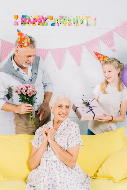 Retrato de mujer feliz delante de marido y nieta con regalos de cumpleaños