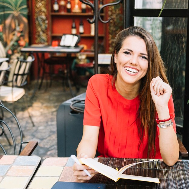 Retrato de una mujer feliz con el diario que se sienta en café