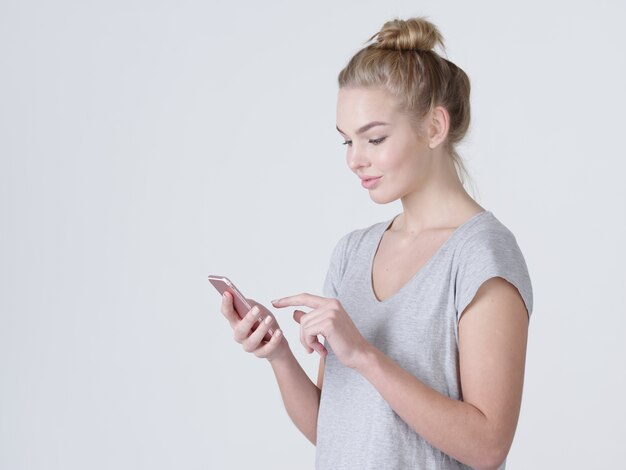 Retrato de una mujer feliz está escribiendo un mensaje de texto en el teléfono móvil - en el estudio