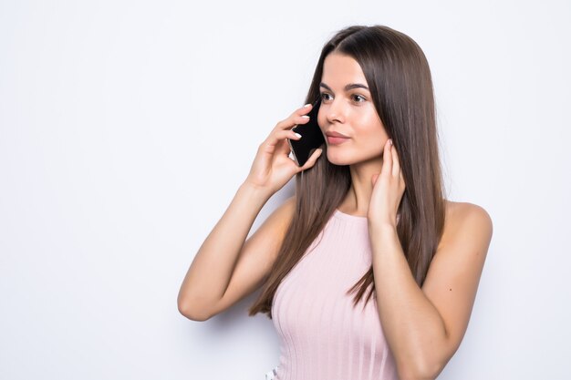 Retrato de una mujer feliz hablando por teléfono sobre una pared blanca.