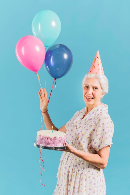 Foto gratuita retrato de una mujer feliz con pastel de cumpleaños y globos sobre fondo azul