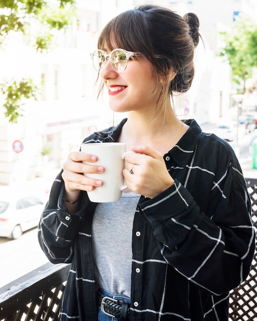 Retrato de una mujer feliz de pie en el balcón con una taza de café