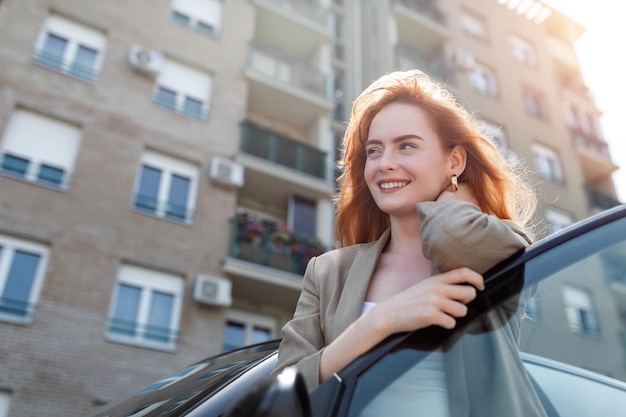 Foto gratuita retrato de mujer feliz de pie junto a un coche en la calle joven mujer bonita de caucasain de pie detrás de un coche con la puerta abierta