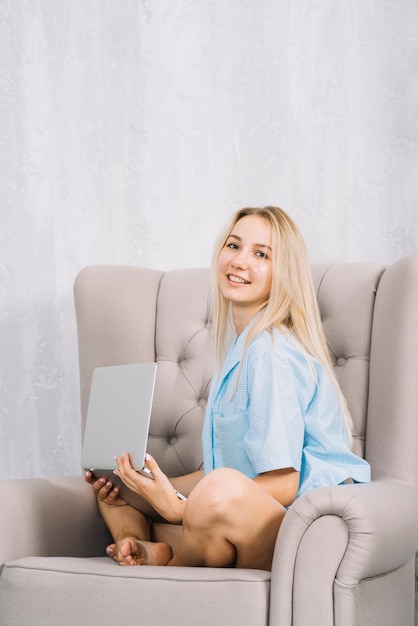 Retrato de una mujer feliz que se sienta en la butaca con la computadora portátil