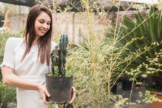 Retrato de una mujer feliz que sostiene la planta en maceta de cactus en invernadero