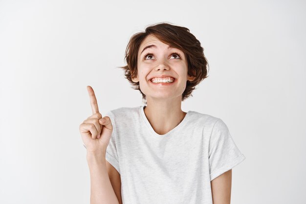 Retrato de una mujer feliz y soñadora señalando la mejor oferta promocional que muestra el logotipo de pie contra el fondo blanco