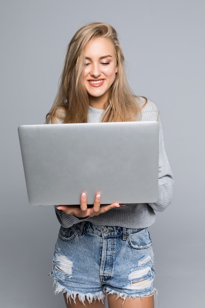 Retrato de una mujer feliz y sorprendida de pie con una computadora portátil aislada sobre un fondo gris