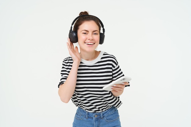 Foto gratuita retrato de una mujer feliz con un teléfono inteligente cambia de canción en una aplicación de transmisión de teléfono móvil escucha música en