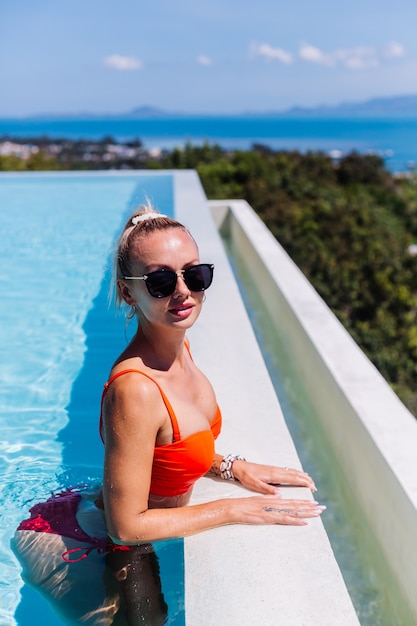 Retrato de mujer feliz tranquila en gafas de sol con piel bronceada en piscina azul en día soleado