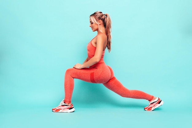 Retrato de mujer fitness en ropa deportiva rosa Modelo hermoso joven con cuerpo perfecto Mujer posando cerca de la pared en el estudio Alegre y feliz Estirándose antes de entrenar