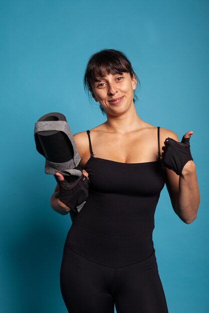 Retrato de una mujer en forma atlética sosteniendo una alfombra de yoga antes de comenzar a trabajar en el entrenamiento de fitness en el estudio. Entrenador personal practicando ejercicios de gimnasia estirando los músculos del cuerpo trabajando en un estilo de vida saludable