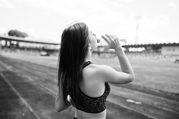 Retrato de una mujer en forma bebiendo agua después de correr en el estadio Foto en blanco y negro