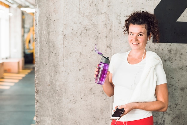 Retrato de una mujer en forma con teléfono inteligente y una botella de agua