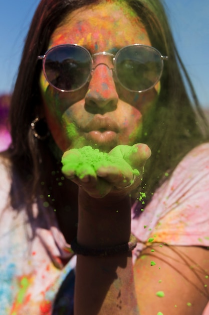 Retrato de una mujer con gafas de sol que sopla el polvo de holi verde