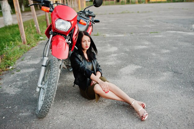 Retrato de una mujer genial e impresionante con chaqueta de cuero negro sentada junto a una bicicleta roja genial