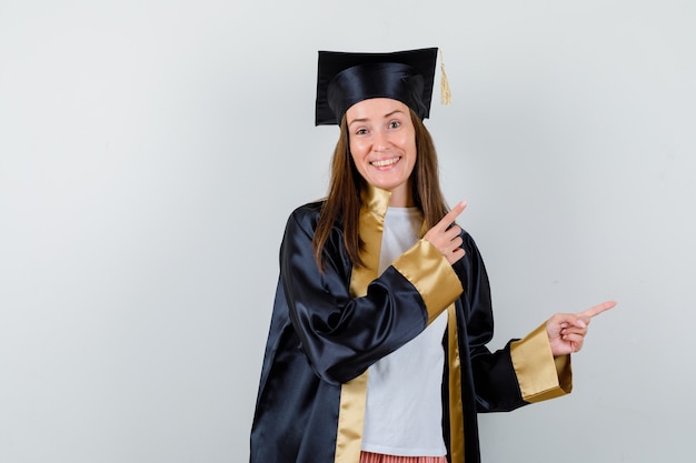 Retrato de mujer graduada apuntando a la esquina superior derecha en traje académico y mirando feliz vista frontal