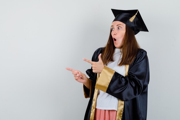 Retrato de mujer graduada apuntando a un lado en ropa casual, uniforme y mirando asombrado vista frontal