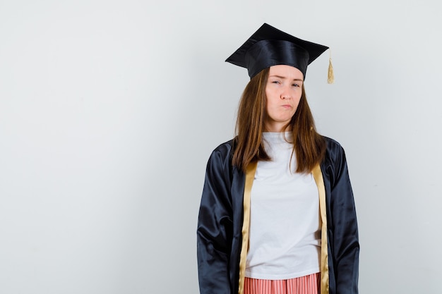 Retrato de mujer graduada mirando a la cámara, labios curvados en traje académico y mirando pensativo vista frontal